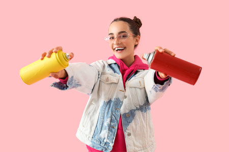Young woman with spray paint cans on pink background
