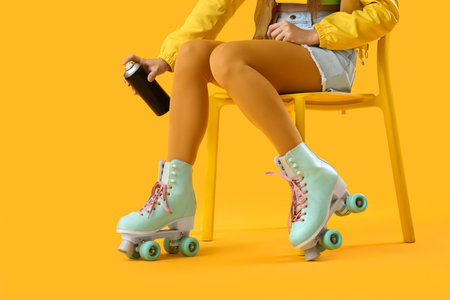Young girl on roller skates and with spray can sitting on chair against yellow backgroundの写真素材