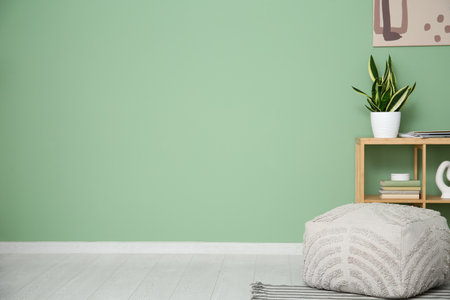 Shelving unit with houseplant and pouf near green wall in roomの写真素材