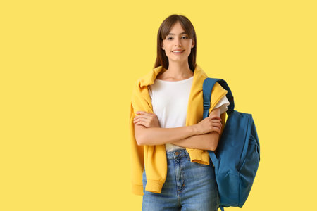 Happy female student with backpack on yellow background