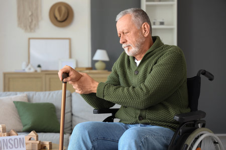 Senior man suffering from Parkinson syndrome with stick in wheelchair at homeの写真素材