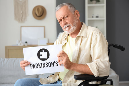 Senior man in wheelchair holding paper with word PARKINSON'S at homeの写真素材