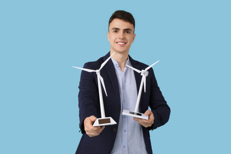 Young businessman with wind turbine models on blue backgroundの写真素材