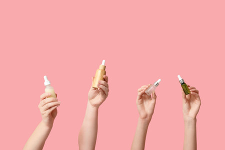 Female hands with bottles of different cosmetic products on pink backgroundの写真素材