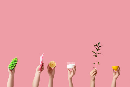Female hands holding cleaning brush, rag, green branch, lemon and jar with cleaning agent on pink backgroundの写真素材