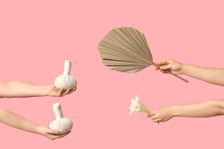 Female hands with herbal massage bags, flower and dried palm leaf on pink backgroundの写真素材