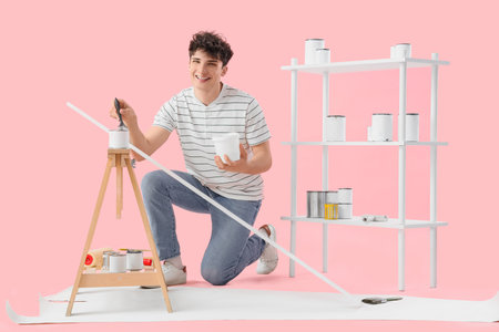 Young man with paint brush and cans on pink backgroundの写真素材