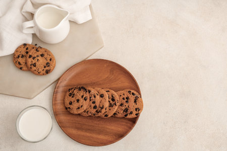 Wooden plate and board of sweet cookies with chocolate chips and glass of milk on white backgroundの写真素材