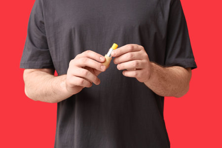 Young man with lip balm on red background, closeupの写真素材