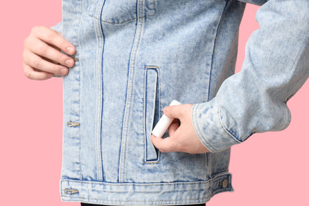 Young man with lip balm in jacket pocket on pink background