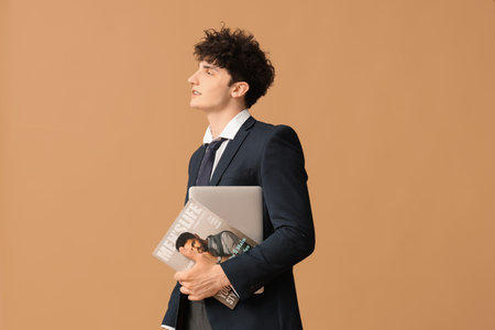 Handsome young businessman with modern laptop and magazine on brown backgroundの写真素材