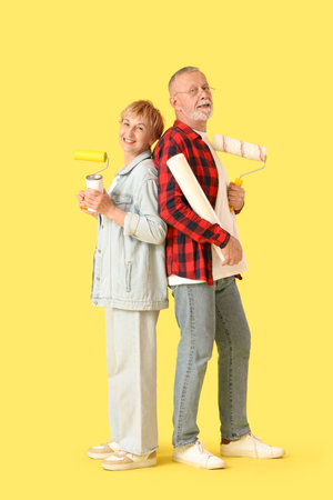 Mature couple with paint cans and rollers on yellow backgroundの写真素材