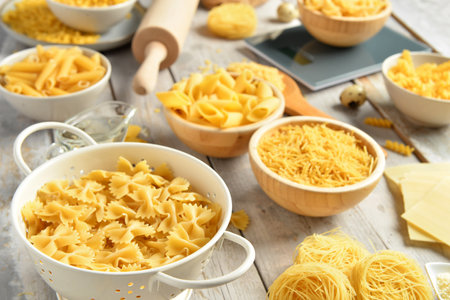 Different types of raw pasta and kitchen utensils on light wooden background, closeupの写真素材