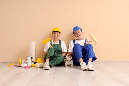 Mature couple of decorators with dog and paint tools sitting near beige wallの写真素材