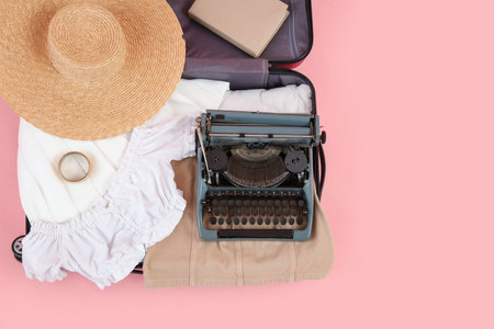 Open suitcase with vintage typewriter and clothes on pink background, top viewの写真素材
