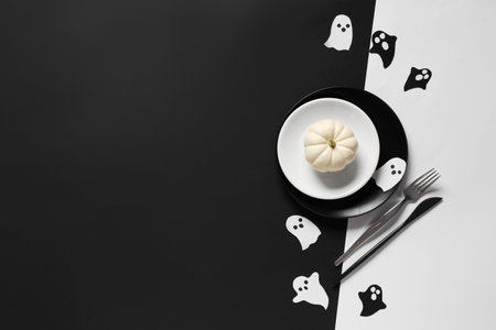Festive table setting for Halloween celebration with paper ghosts and pumpkin on color background