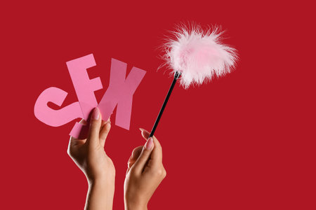 Woman with the word SEX and feather stick on red backgroundの写真素材