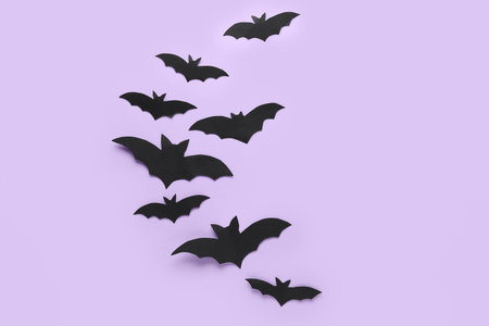 Black paper bats for Halloween party on lilac background