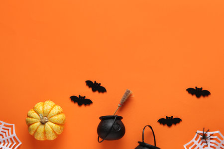 Black bats with paper spider web, cauldrons and fresh pumpkin for Halloween party on orange backgroundの写真素材