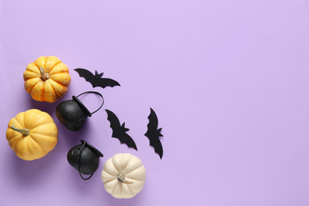 Paper bats with cauldrons and fresh pumpkins for Halloween party on lilac backgroundの写真素材