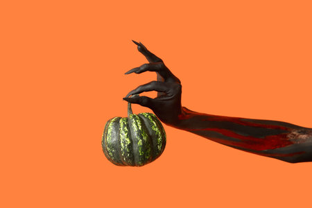 Black witch hand with claws and green pumpkin on orange background. Halloween celebrationの写真素材