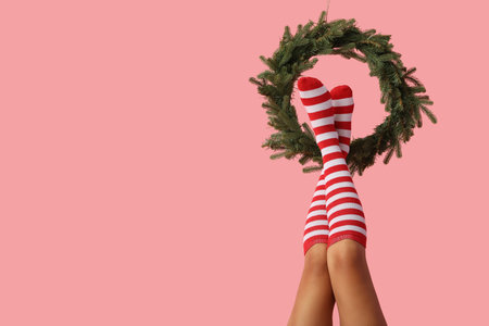 Legs of sexy young woman in Christmas stockings with wreath on pink backgroundの写真素材