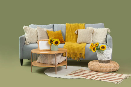 Gray sofa with sunflowers, table and pouf on green background