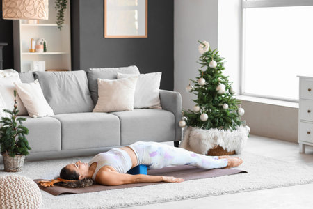 Sporty mature woman in reindeer horns with block doing yoga at home on Christmas Eveの写真素材