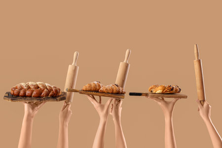 Female hands holding wooden boards with different tasty pastry and rolling pins on beige backgroundの写真素材