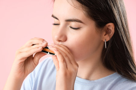 Young woman playing harmonica on pink background, closeupの写真素材