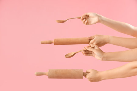Female hands with wooden rolling pins and spoons on pink backgroundの写真素材