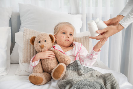 Little girl ill with chickenpox taking pills from her mother in bedroomの写真素材