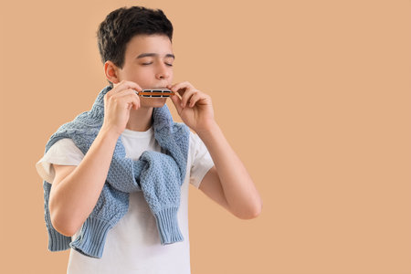 Teenage boy playing harmonica on beige backgroundの写真素材