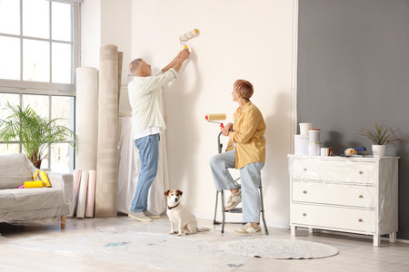 Mature couple with dog painting wall during repair in their new houseの写真素材