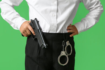 Teenage police officer with gun and handcuffs on green backgroundの写真素材