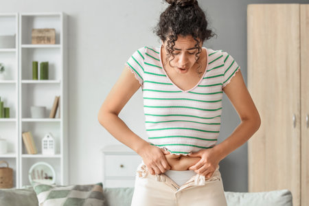 Young African-American woman in tight pants at home. Diet conceptの写真素材