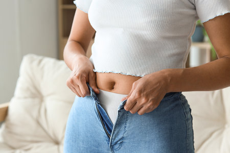 Young woman trying to button tight pants at home, closeup. Diet conceptの写真素材