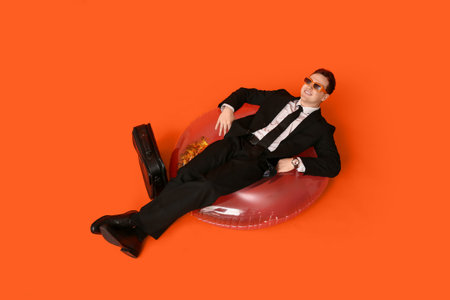 Office worker lying in inflatable ring dreaming about vacation on orange backgroundの写真素材