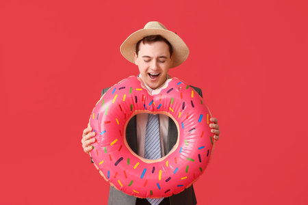 Office worker with inflatable ring in shape of donut dreaming about vacation on red backgroundの写真素材