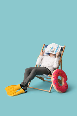 Office worker sitting on deck chair with newspaper and dreaming about vacation on blue backgroundの写真素材