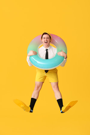 Office worker with inflatable ring and flippers dreaming about vacation on yellow backgroundの写真素材