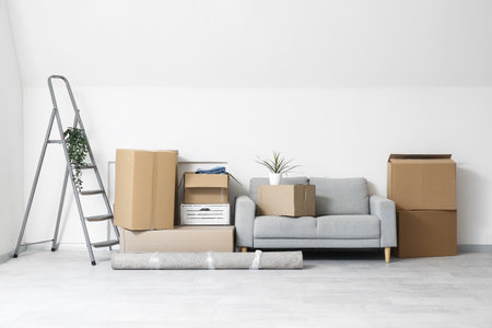 Gray sofa and cardboard boxes near white wall in light living room on moving dayの写真素材