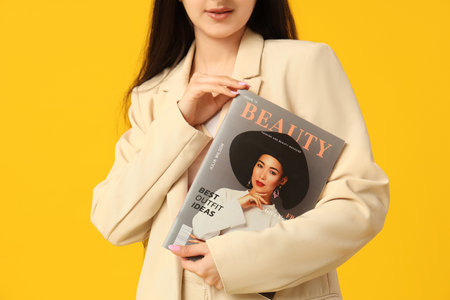 Beautiful young woman with magazine on yellow background, closeupの写真素材