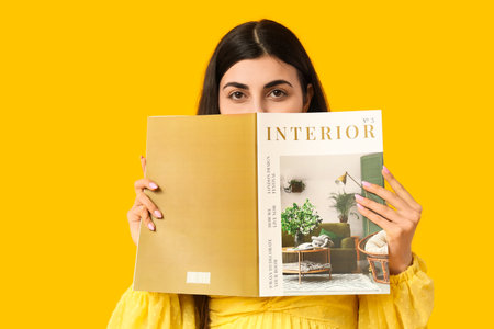 Beautiful young woman reading magazine on yellow backgroundの写真素材