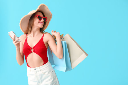 Beautiful young woman with shopping bags using mobile phone on blue backgroundの写真素材