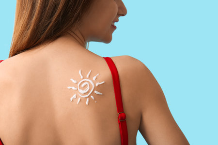 Young woman with sunscreen cream on her shoulder on blue backgroundの写真素材