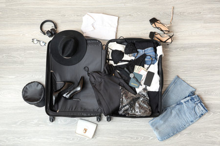 Open suitcase with female clothes, mobile phone and passport on floor. Travel concept