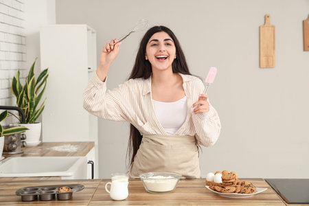 Beautiful young happy woman preparing dough for tasty cookies with chocolate chips in kitchen