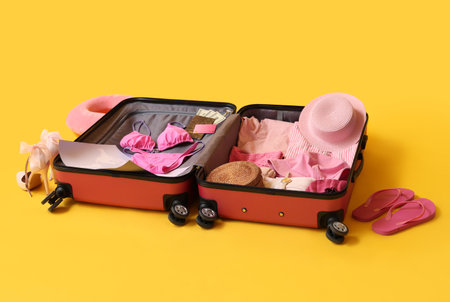 Open suitcase with female pink clothes, map and passport on yellow background. Travel conceptの写真素材
