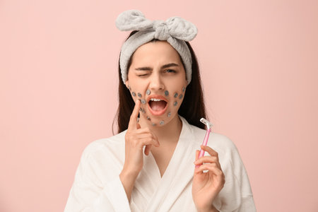 Beautiful young shocked woman with razor and drawing pins on pink background. Depilation conceptの写真素材